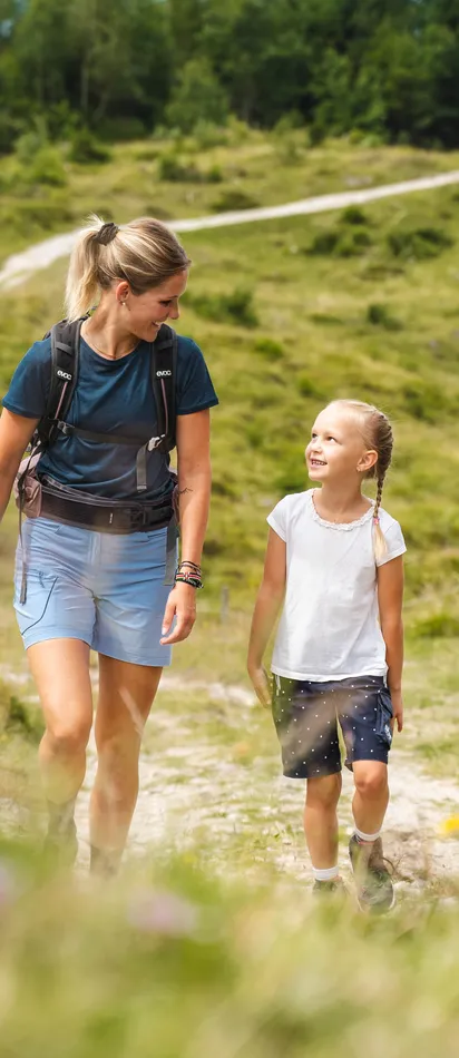 Family hiking on mountain trail through green meadow on a sunny day