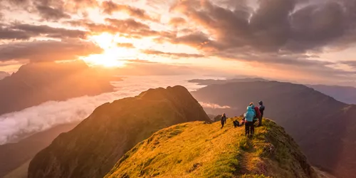 Wanderer auf einem Bergkamm bei Sonnenaufgang mit dramatischen Wolken und Talblick
