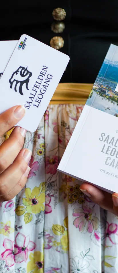 Woman in traditional dress holding Saalfelden Leogang Card and brochure for 2024–2025