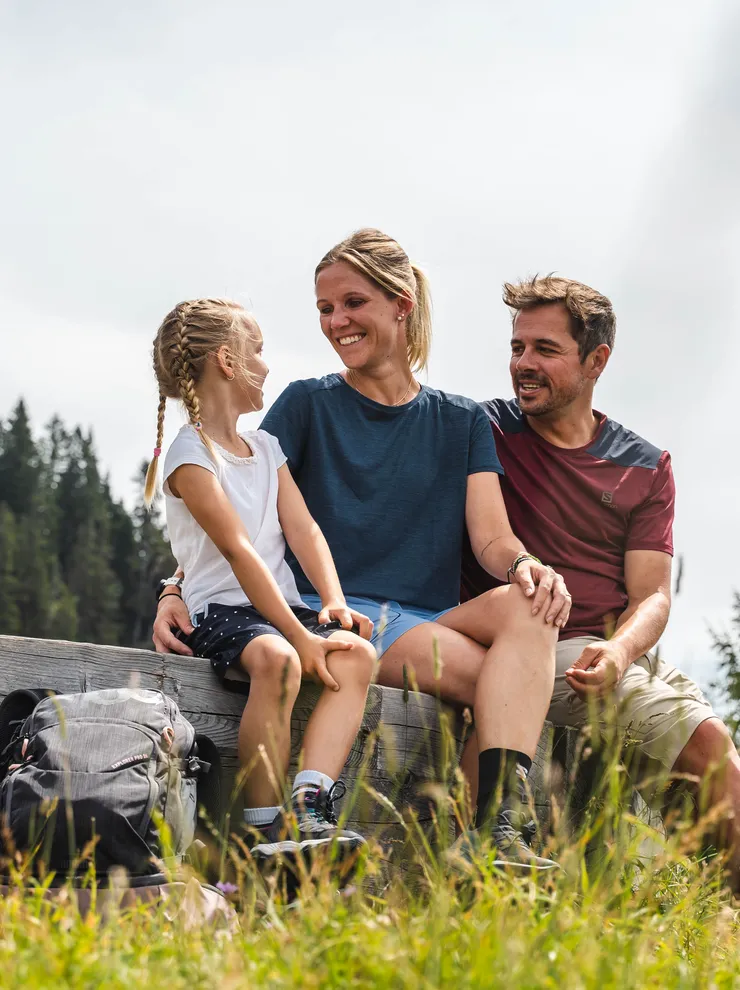 Smiling family sitting on a bench during a summer hike in the mountains
