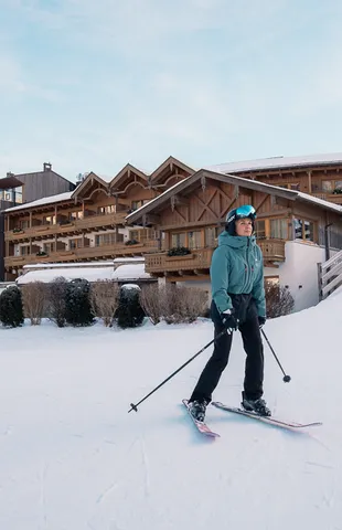 Skifahrer auf verschneiter Piste vor einem alpinen Skigebiet mit Chalets aus Holz