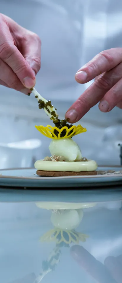 Pastry chef plating gourmet dessert with yellow sugar decoration and spoonful of garnish