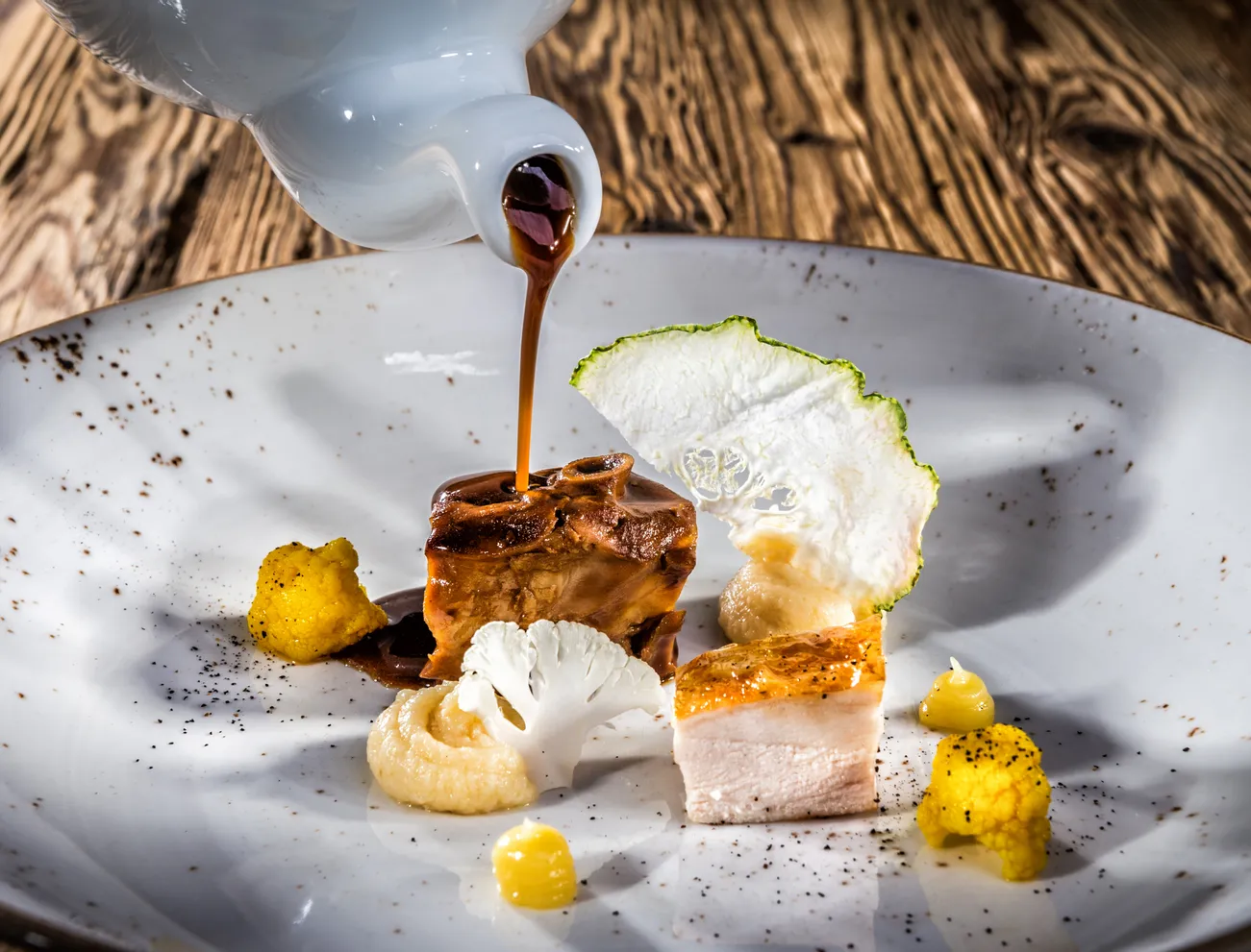 Gourmet-Hähnchengericht mit Sauce, Blumenkohlpüree und Gemüsegarni auf rustikalem Teller