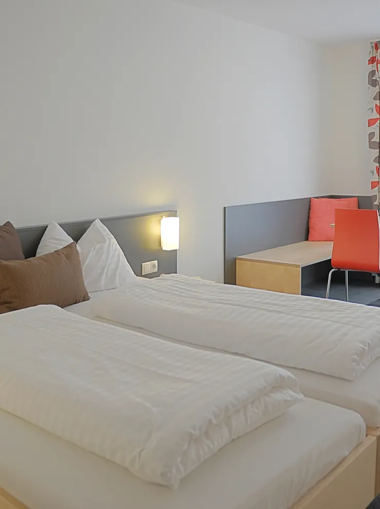 Modern hotel room with double bed, seating area, and bright natural light