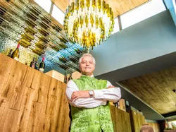 Man in green traditional vest standing proudly beneath chandelier made of wine bottles