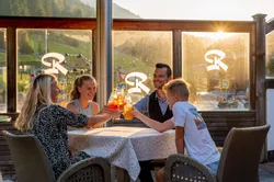 Family toasting drinks together at a mountain restaurant terrace during sunset