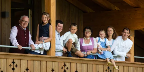 Lächelnde Mehrgenerationenfamilie auf einem alpinen Holzbalkon in traditioneller österreichischer Kleidung