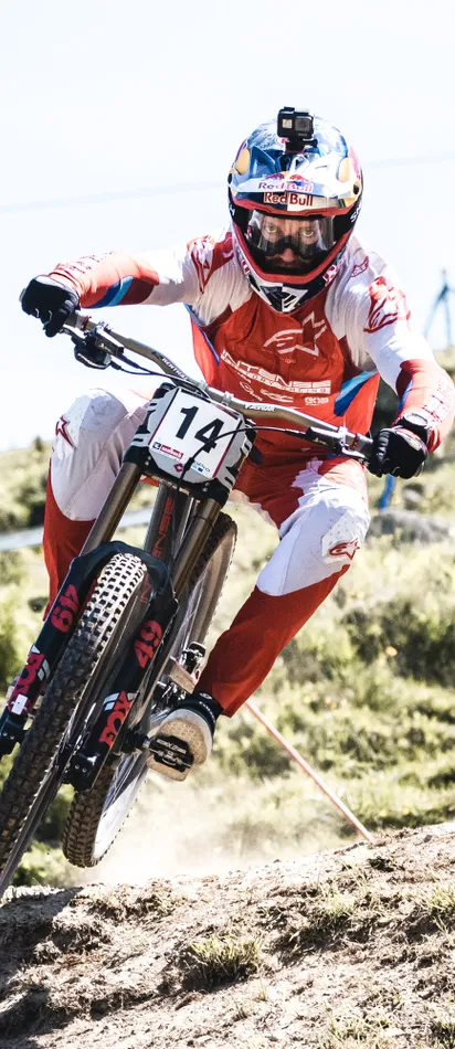Downhill mountain biker racing on rocky trail wearing red gear and helmet with GoPro