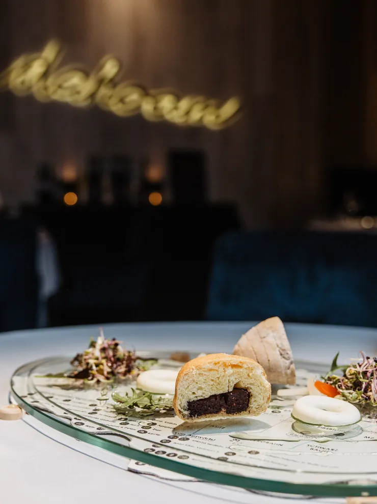 Gourmetgericht mit Salat, Brot und Bier auf moderner Glasplatte im Fine-Dining-Restaurant