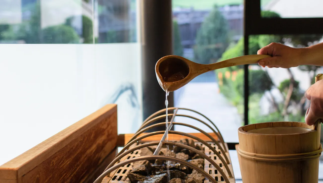 Pouring water on hot sauna stones with wooden ladle and bucket in modern spa