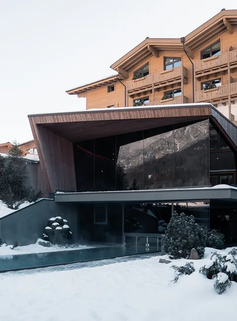 Modernes Alpenhotel mit Außenpool umgeben von Schnee in winterlicher Landschaft