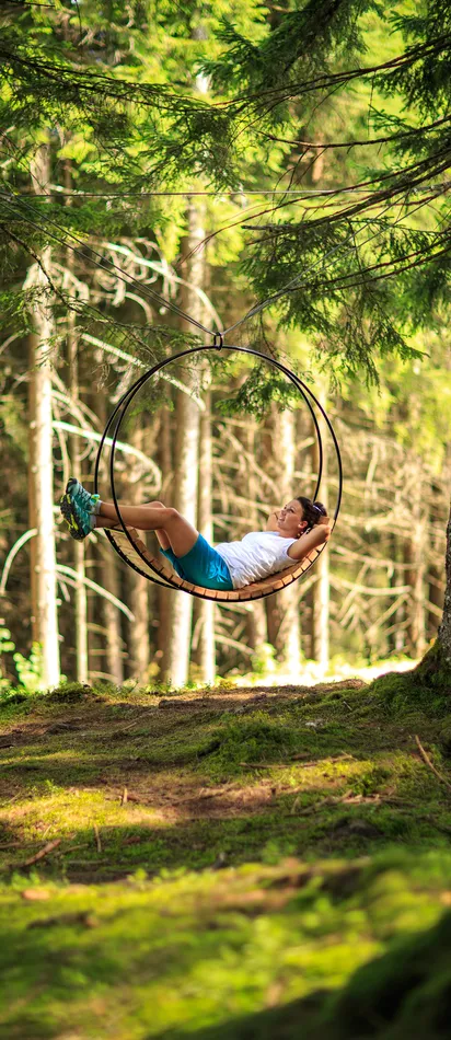 Woman relaxing on a hanging circular swing in a sunlit forest