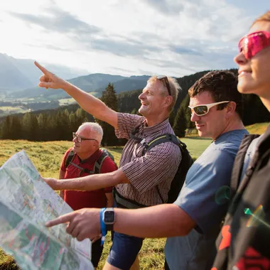 Wandergruppe liest Karte und zeigt auf Berge in alpiner Landschaft