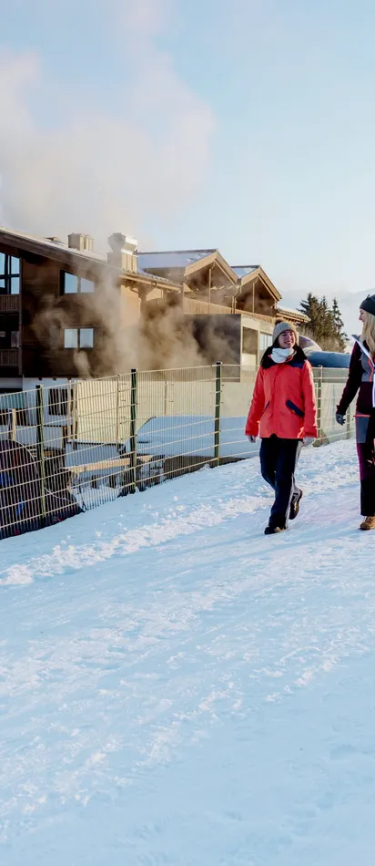 Two women walking on snowy path near alpine chalet in winter mountains
