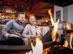 Glückliches Paar entspannt am Kamin mit Getränken in einer rustikalen Almhütte