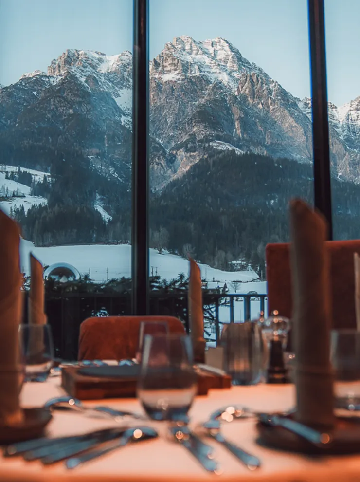 Elegant gedeckter Restauranttisch mit Blick auf schneebedeckte Alpen durch großes Fenster