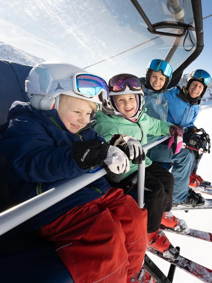 Family with ski gear riding a chairlift in sunny mountain ski resort