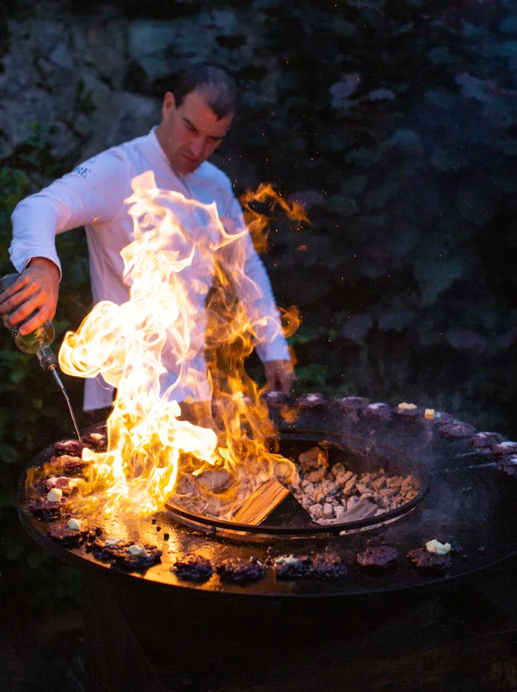 Koch grillt Blaubeer-Nocken über offenem Feuer mit Flammen an einem Outdoor-Grill