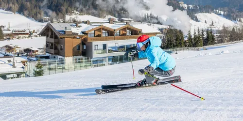 Skifahrer in blauer Jacke carvt eine präparierte Piste mit schneebedeckten Alpen im Hintergrund hinunter