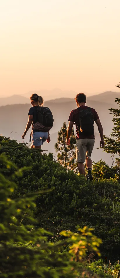Paar wandert bei Sonnenuntergang auf einem Bergpfad zwischen Kiefern und Hügeln