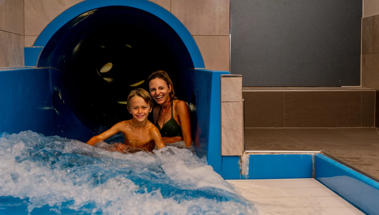 Lächelnde Mutter und Kind rutschen aus einer Indoor-Wasserrutsche im Wasserpark
