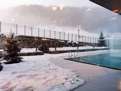 Beheizter Außenpool im Winter mit Weihnachtsbäumen und verschneiter Berglandschaft