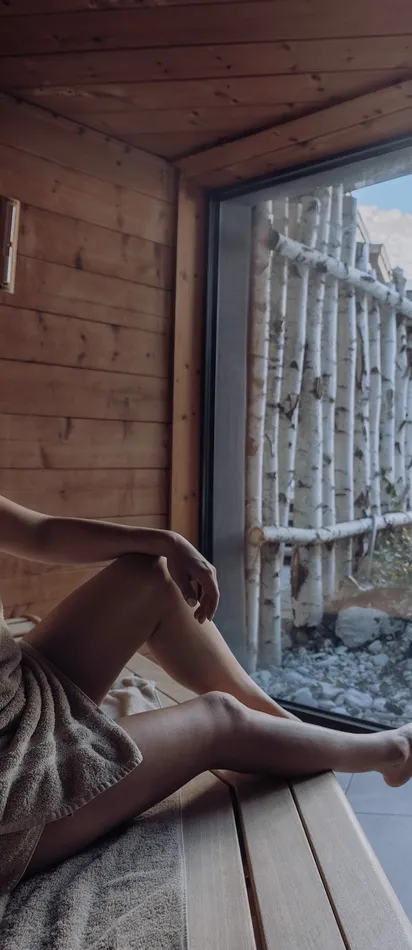 Woman relaxing in sauna with scenic snowy mountain view through large glass window