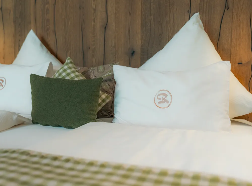 Cozy hotel bed with white pillows, green cushions and wooden headboard