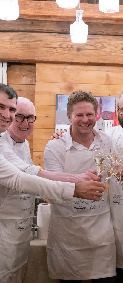 Group of chefs toasting with white wine glasses in rustic restaurant setting
