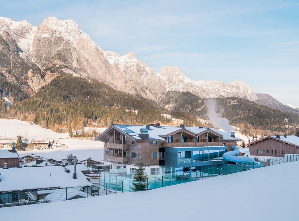 Modernes Alpenhotel mit Außenpool und Wasserrutsche im verschneiten Bergdorf