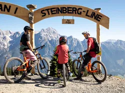 Family on mountain bikes at Steinberg Line trailhead with alpine mountains in background
