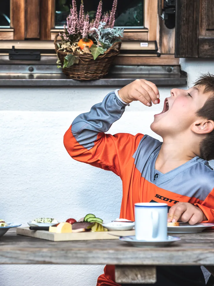 Zwei Jungen essen Obst an einem Holztisch im Freien mit Frühstückstellern