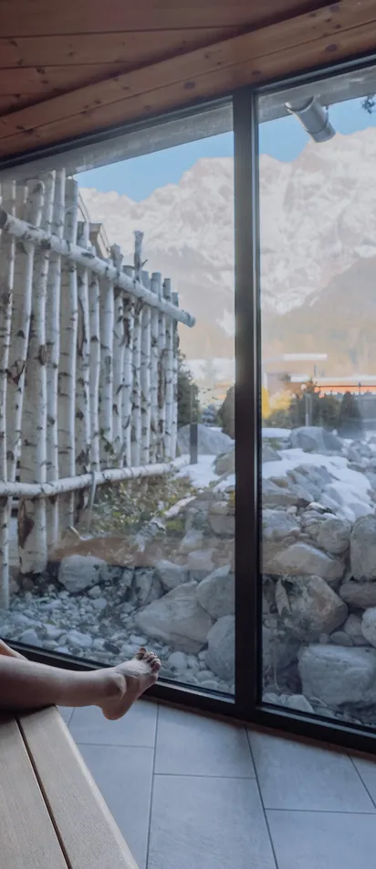 Woman relaxing in a wooden sauna with panoramic view of snowy mountain landscape
