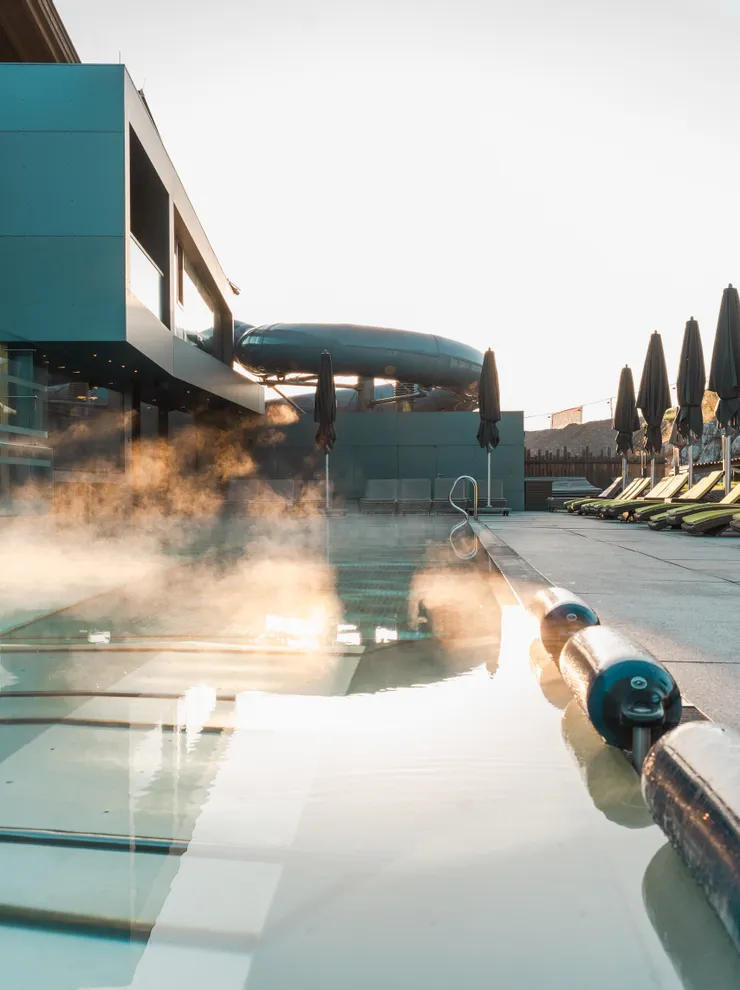 Steam rising from heated outdoor pool beside modern hotel terrace with lounge chairs