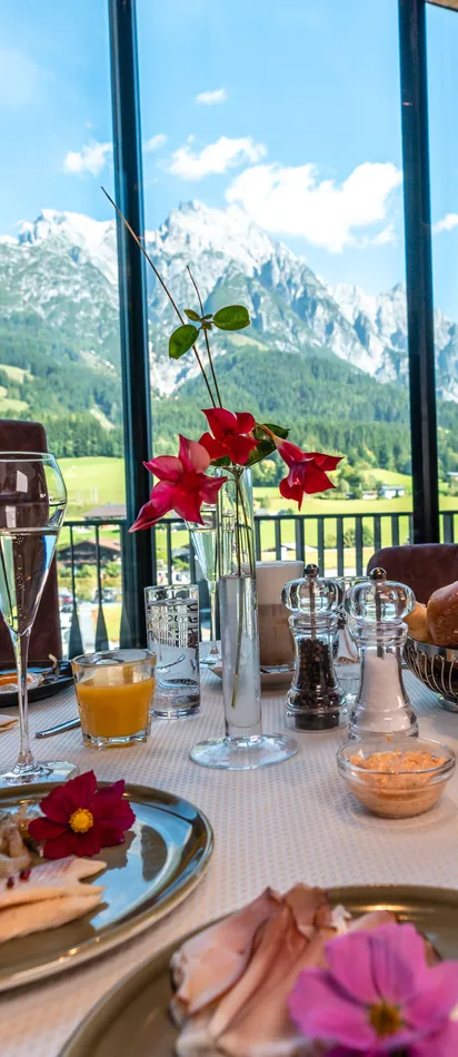 Luxuriöses Frühstück mit Gebäck, Obst und Schinken vor Bergpanorama in einem Alpenhotel