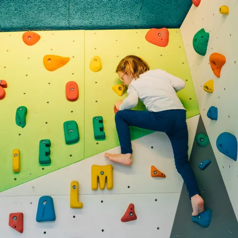 Kind klettert an Indoor-Boulderwand mit bunten Griffen in Buchstabenform