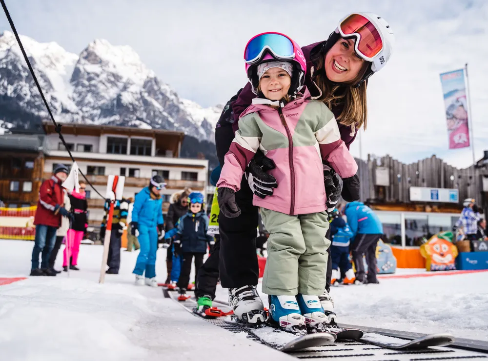 Lächelndes Kind lernt mit Skilehrerin Skifahren auf verschneitem Hang im Skigebiet