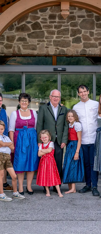 Family in traditional attire standing in front of hotel entrance with flowers and stone wall