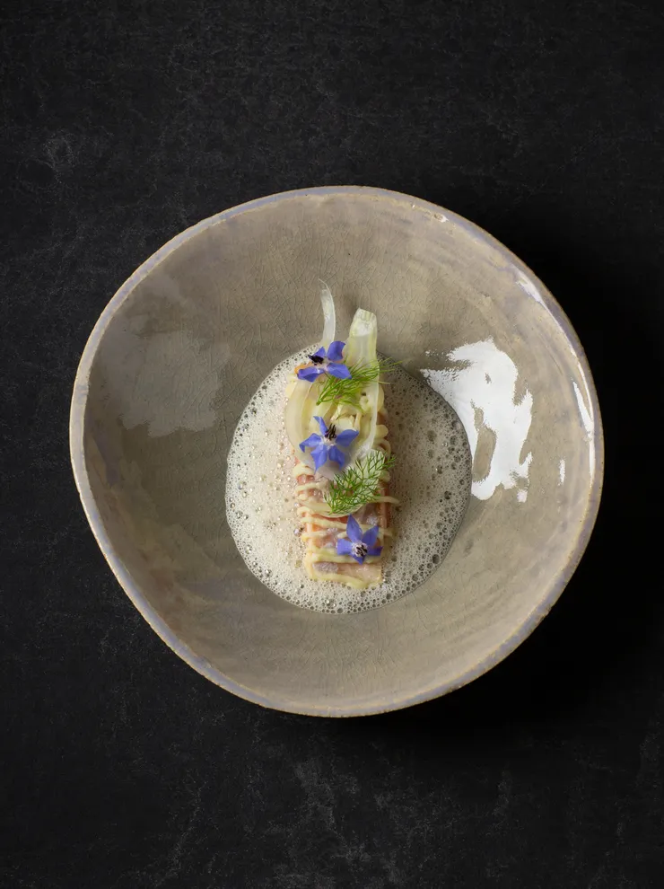 Gourmet pasta dish with foam garnish, fennel, and edible blue flowers in ceramic bowl