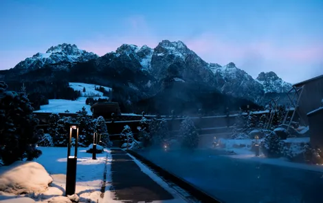Heated outdoor pool in snowy mountain resort at dusk with scenic alpine backdrop