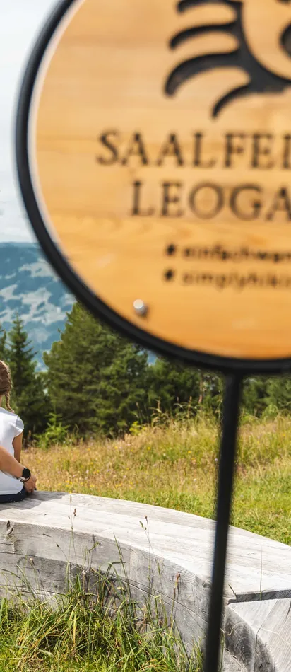 Family sitting on wooden bench overlooking mountains in Saalfelden Leogang during hike