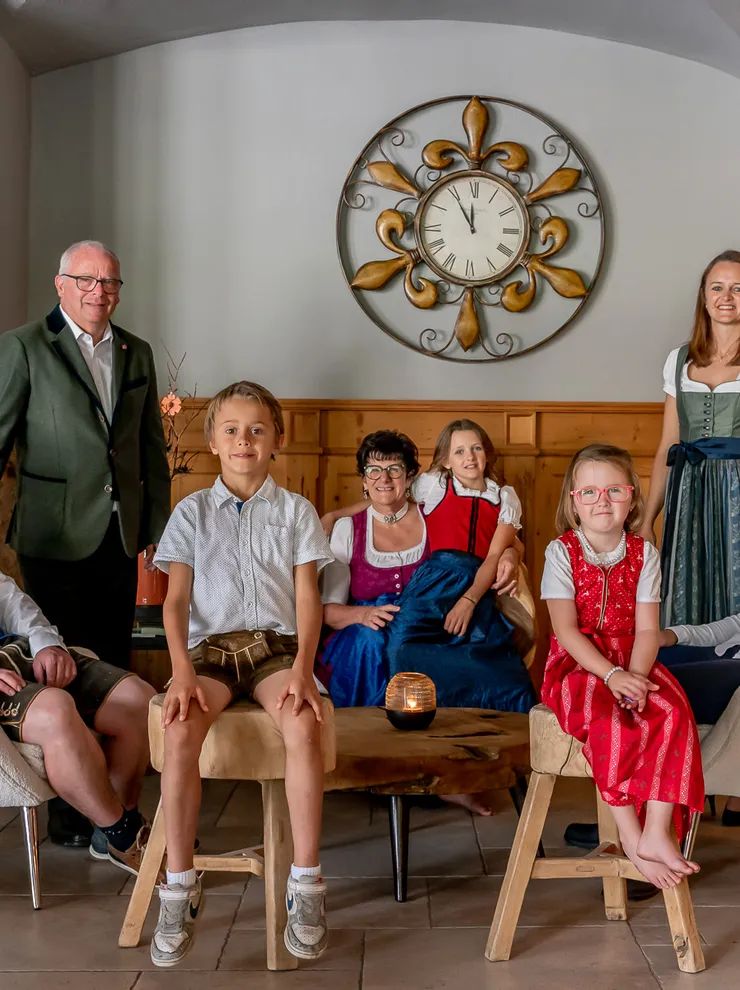 Familienfoto in traditioneller Tracht in gemütlichem Wohnzimmer mit großer Wanduhr