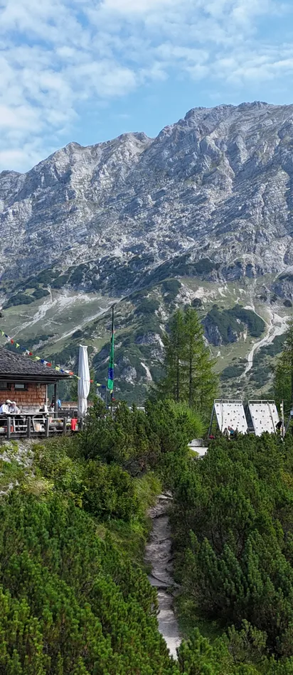 Berghütte mit Terrasse in den Alpen, umgeben von Bäumen und felsigen Gipfeln