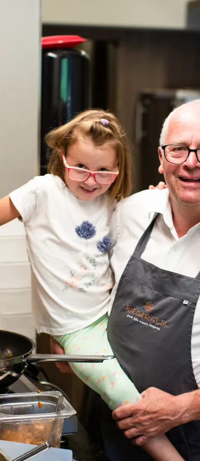 Smiling chef holding child stirring food in pan in professional kitchen