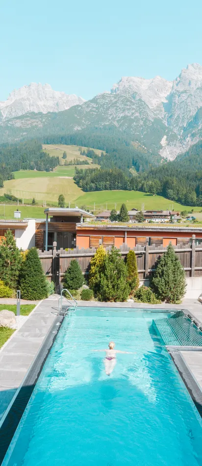 Außenpool mit Liegestühlen vor Alpenkulisse in sonniger Hotelanlage