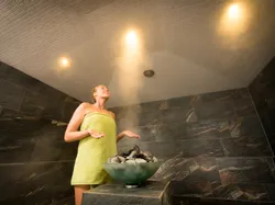 Woman relaxing in a modern steam sauna with heated stones and tiled walls
