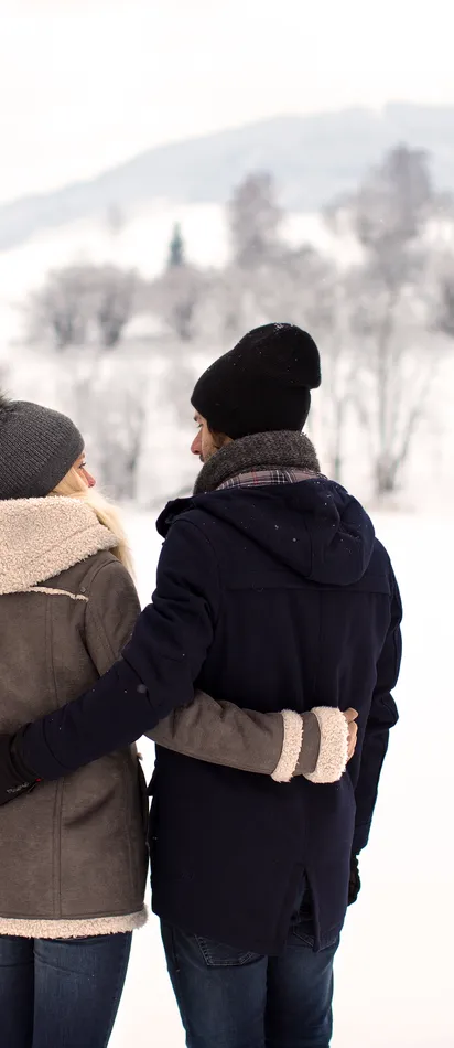 Couple in winter jackets embracing each other in snowy landscape with hills
