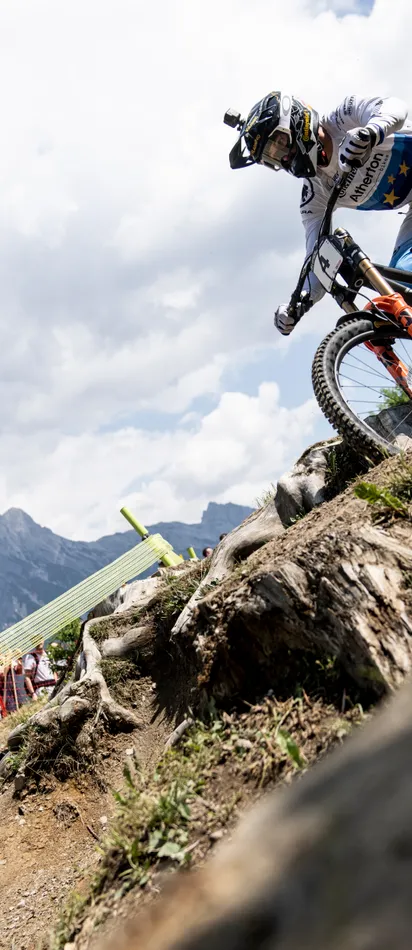 Mountainbike-Rennfahrer fährt einen felsigen Trail bei einem Wettbewerb in den Alpen mit jubelndem Publikum