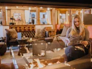 Woman reading a menu in a cozy lounge with fireplace and rustic wooden decor