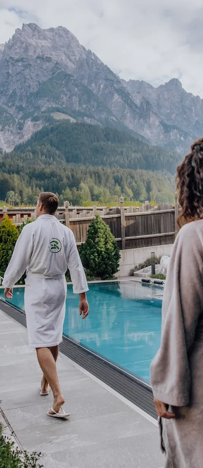 Paar in Bademänteln am Außenpool eines Alpen-Wellnesshotels mit Bergblick
